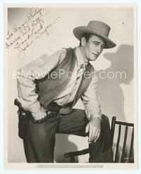 7f060 JOHN WAYNE signed 8x10 still '40s great cowboy portrait standing with one foot on chair!