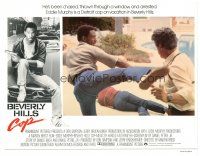 3e209 BEVERLY HILLS COP English LC '84 great close up of cop Eddie Murphy kicking bad guy!