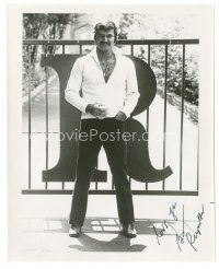 5a453 BURT REYNOLDS signed 8x10 still '70s c/u standing in front of the gate to his house w/ drink!