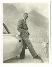 7d072 GOLDFINGER 7.75x10 still '64 Sean Connery as James Bond leaning on cool Aston Martin car!