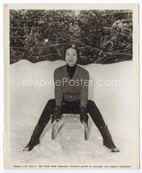 1b039 CAPUCINE 8.25x10.25 '63 great publicity shot of her sitting on a sled outside in the snow!