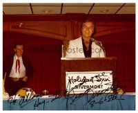 3z437 GEORGE MONTGOMERY signed color 8x10 publicity still '86 speaking at podium at Holiday Inn!