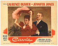 8g614 CARRIE LC #1 '52 Laurence Olivier stands behind Jennifer Jones as she puts on hat!
